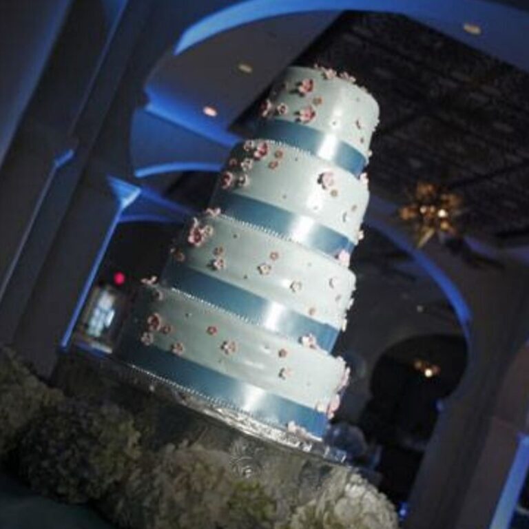 A wedding cake that is spotlit. Blue uplights are in the background