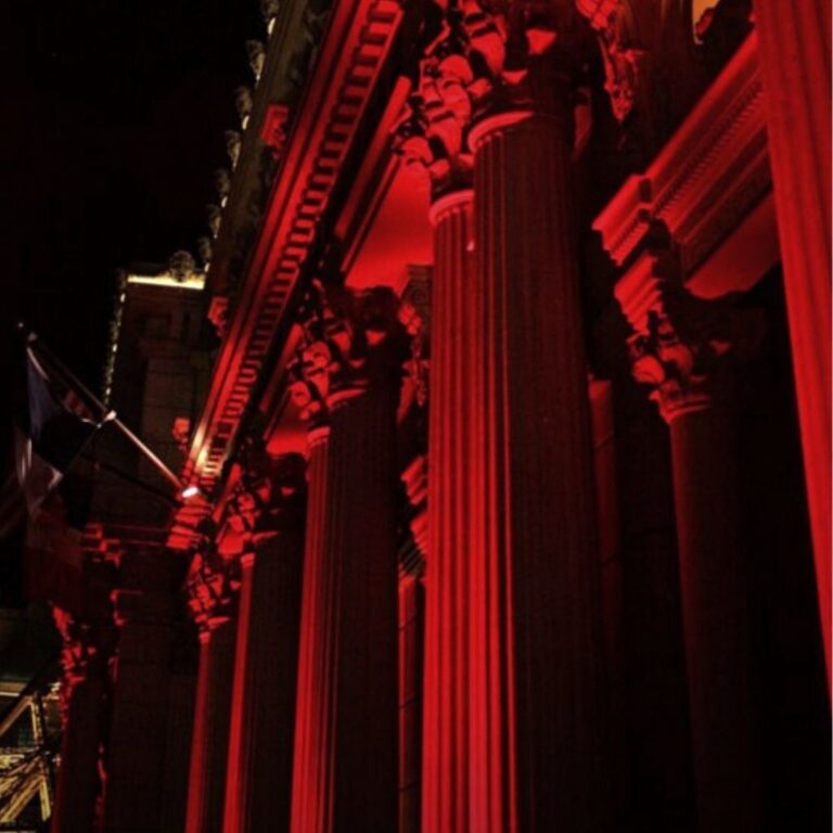Large outdoor building pillars lit with red uplights at night.