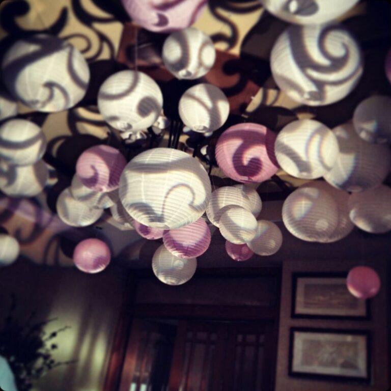 Pink and white paper lanterns hung for a wedding. Swirl gobo patterns are projected on them.